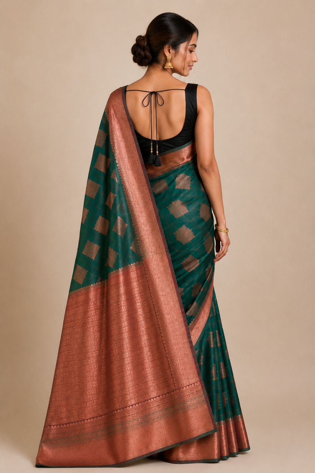 A woman shown from the back wearing a dark green silk saree with a coppery bronze border.