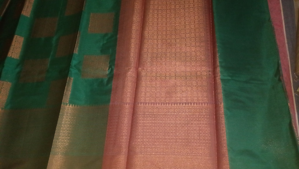 A dark green silk saree with a metallic copper-pink border and pallu.