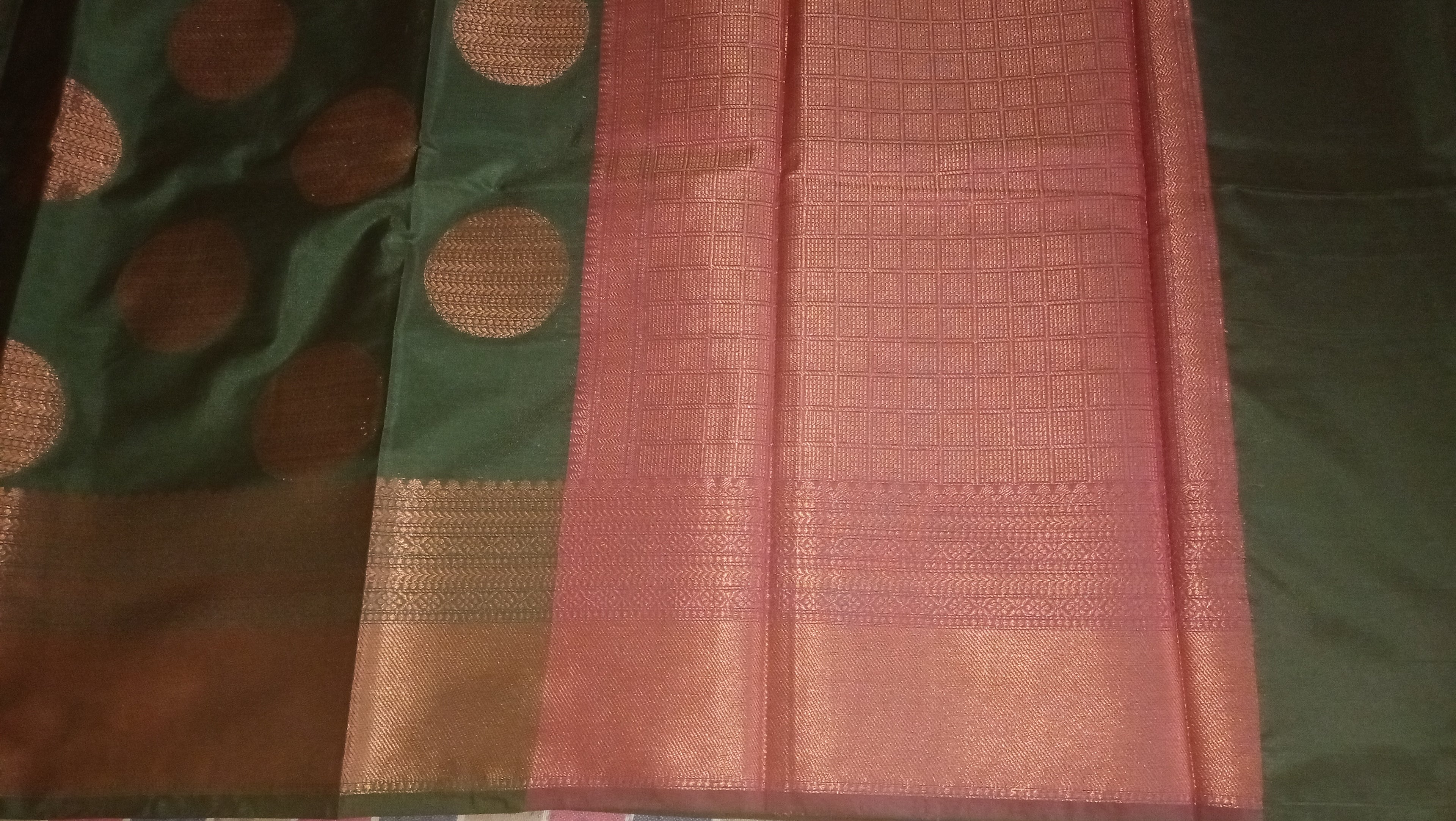 A dark green silk saree with gold motifs and a wide pink border.