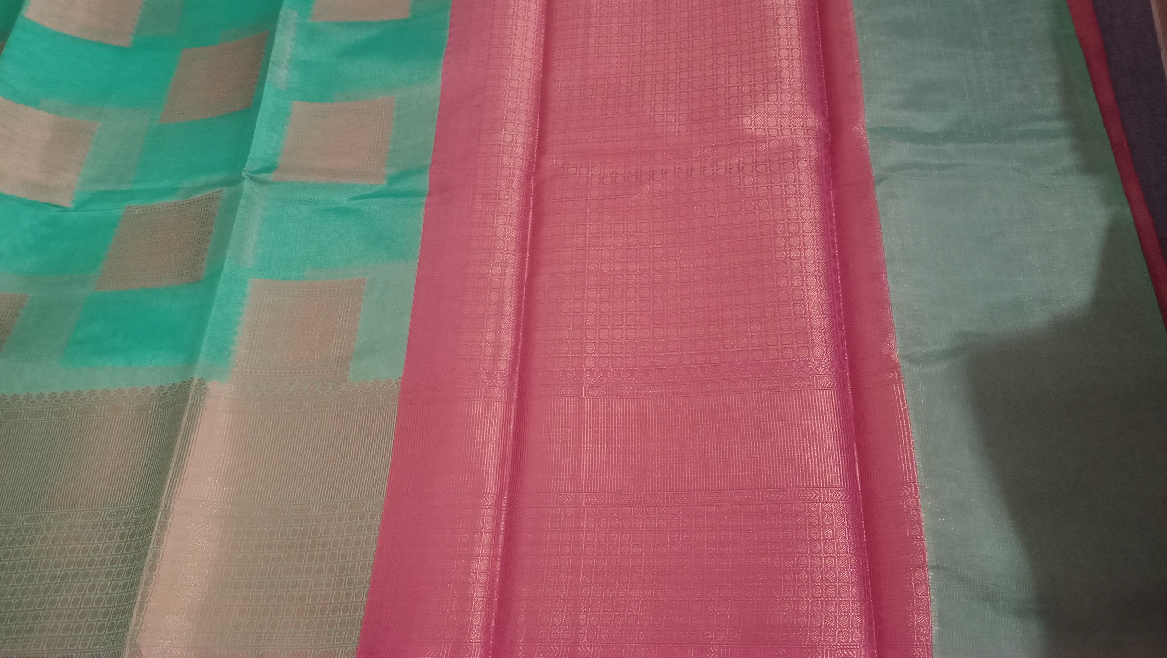 A close-up of a pink and mint green checkered fabric saree or scarf, showing its woven texture and pattern. 