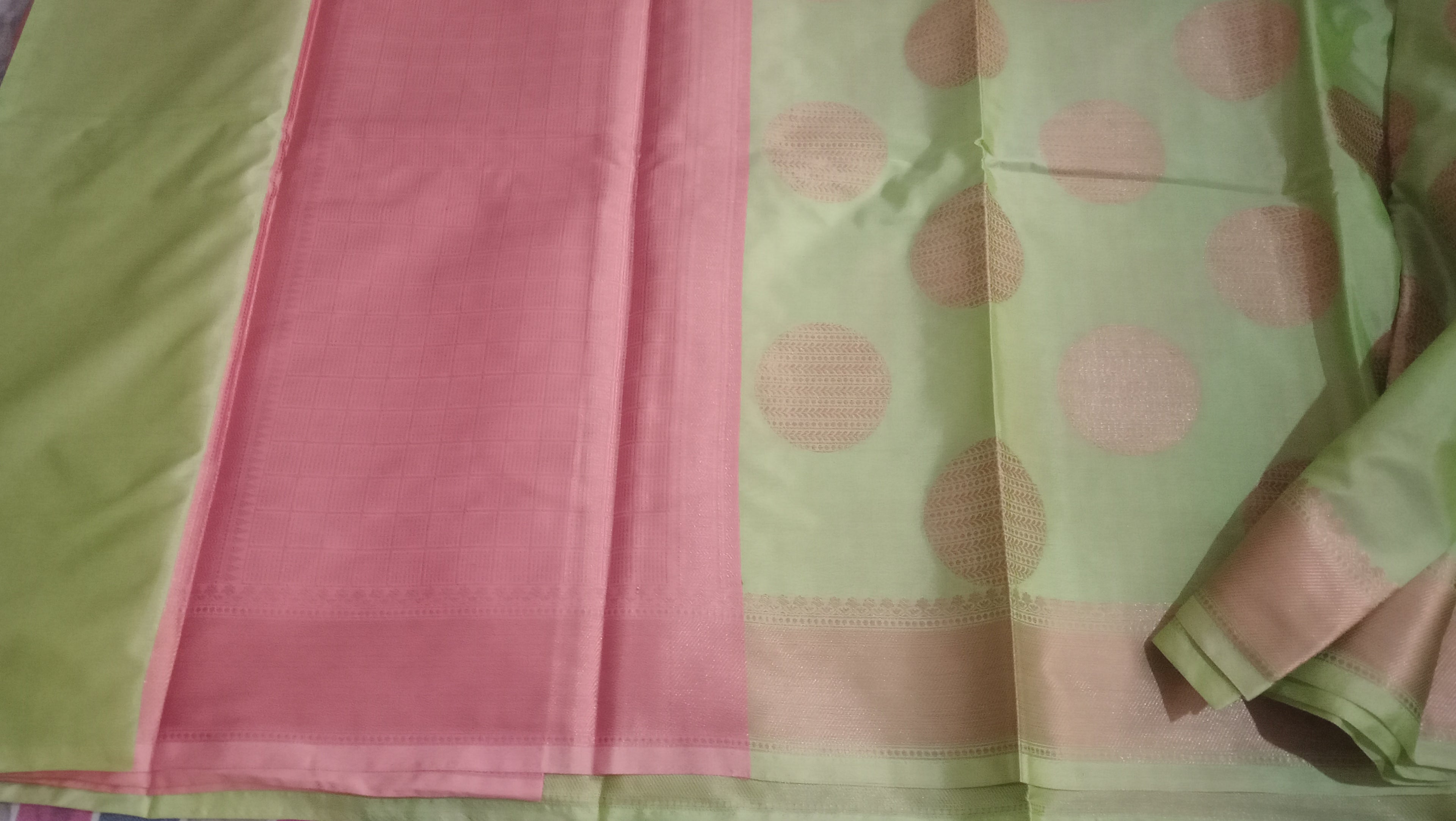 A folded light green saree with pink polka dots and a solid pink border, displayed on a white background. 