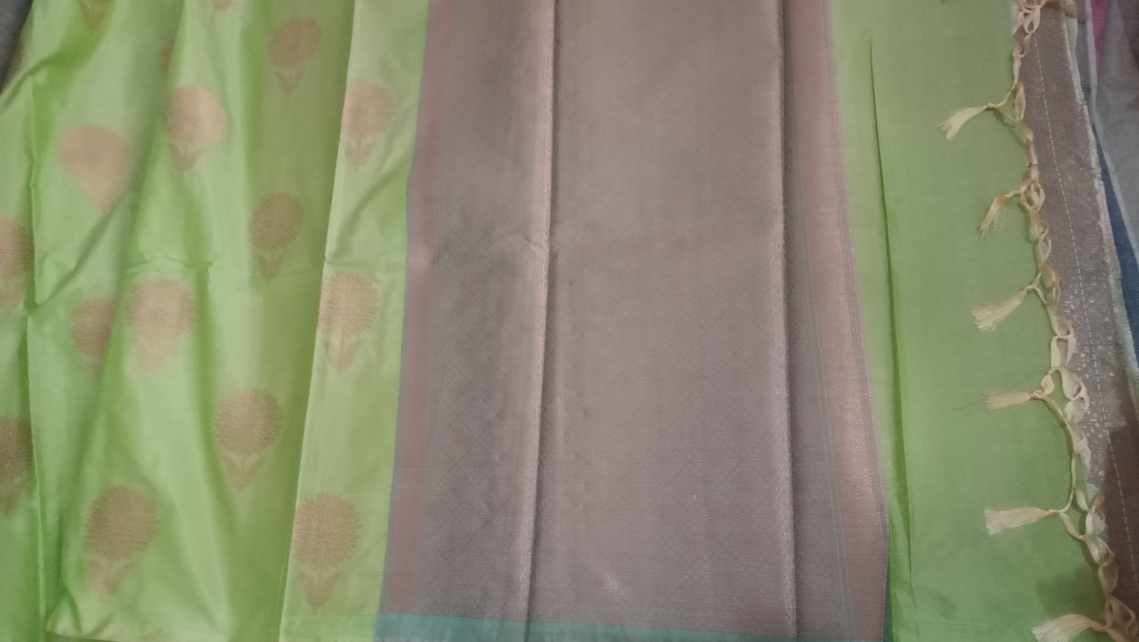 A close-up of a light green fabric with beige floral motifs, and a decorative tassel trim on the right side.