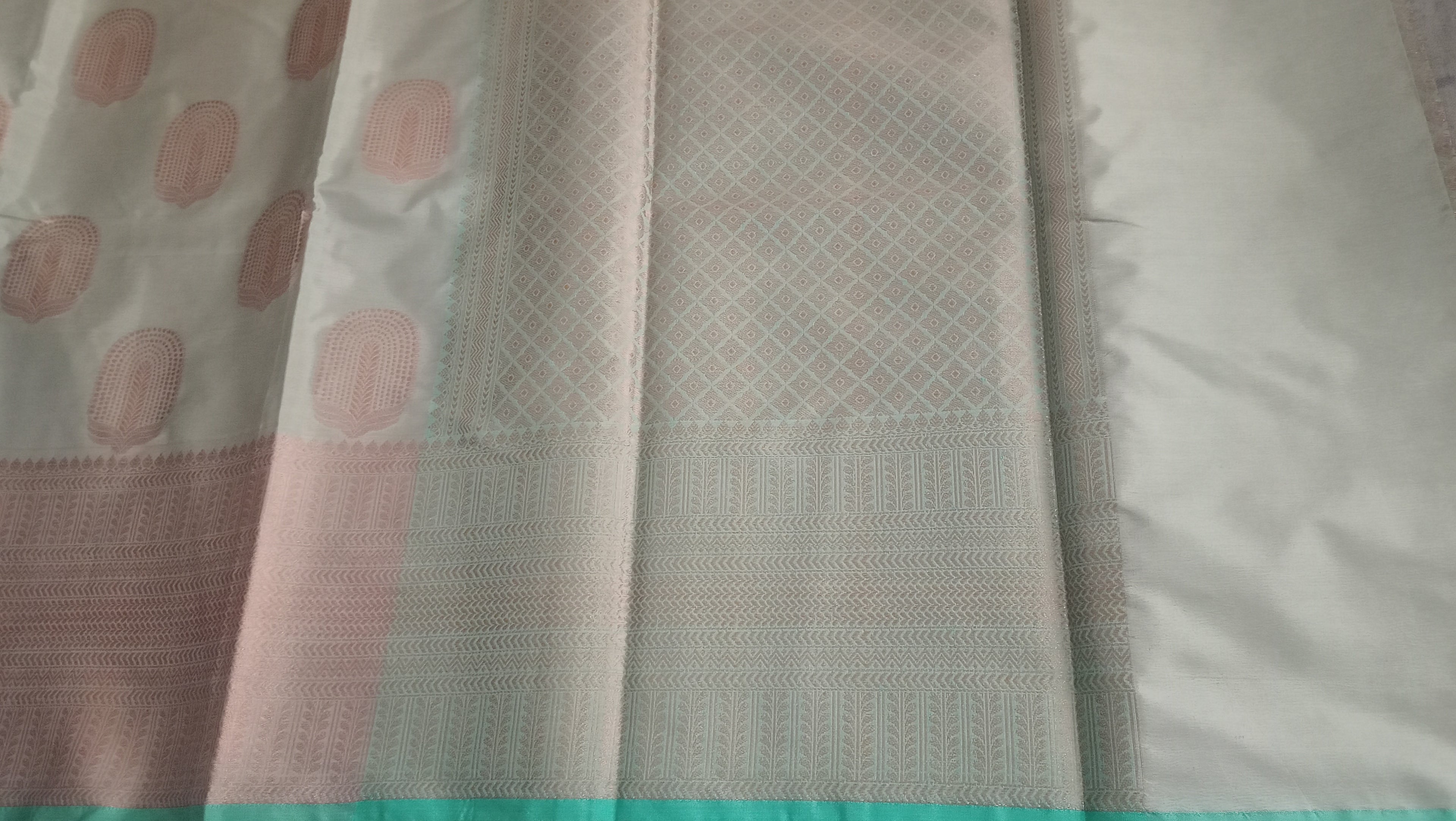A close-up of a light-colored fabric saree, and a subtle silver border.  