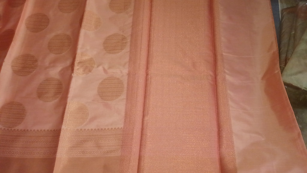 A peach-pink silk saree with a wide border featuring large gold circular motifs, shown folded. 