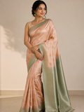 A woman modeling a peach and sage green silk saree with a matching sleeveless blouse, standing against a neutral beige wall.