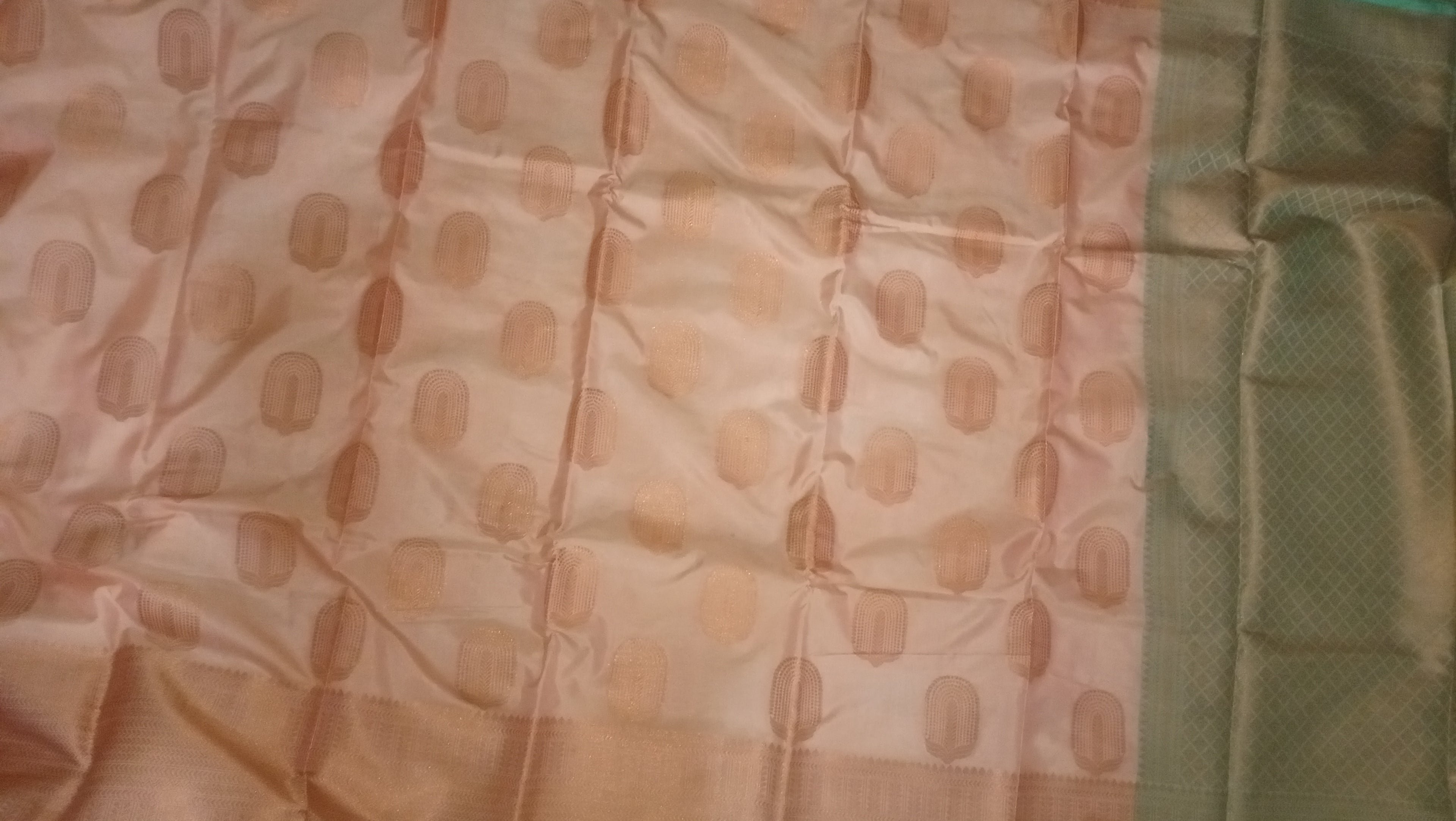 A close-up of a fabric textile with a light peach-beige base, repeating muted peach oval motifs, and a contrasting sage green aachal on the right side.