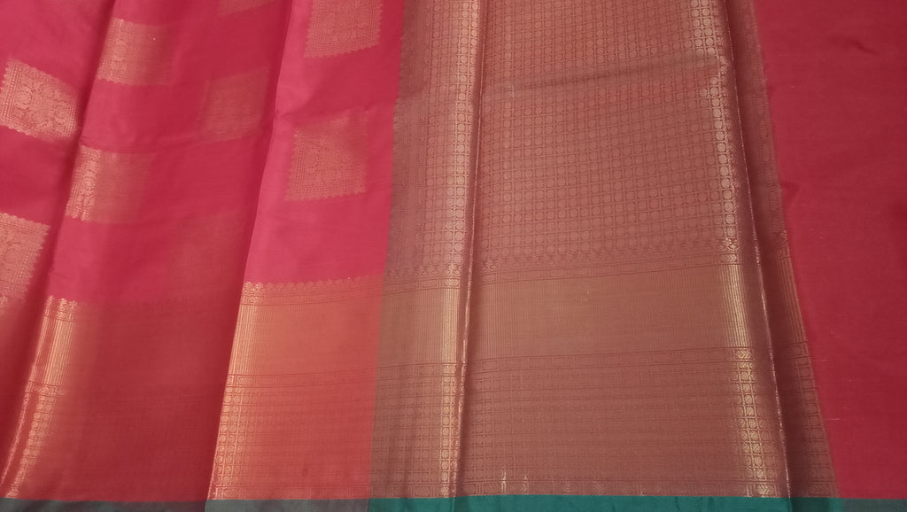 A close-up of a red saree or fabric panel with metallic patterns and a teal border at the bottom. 