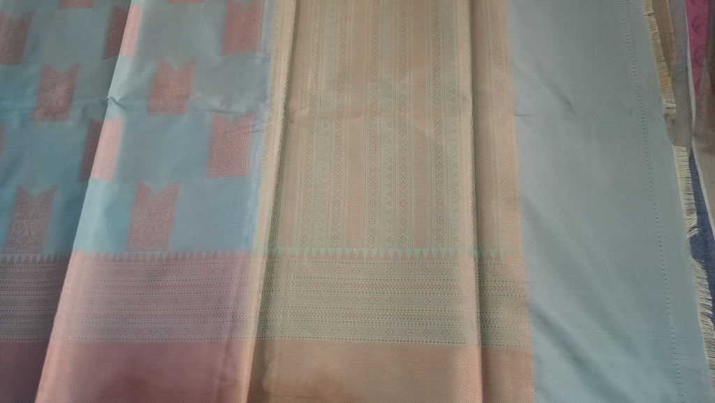 A close-up of a draped fabric, likely a saree, featuring a light blue body with pink and gold woven motifs, a central beige and gold striped border, and a light blue pallu.