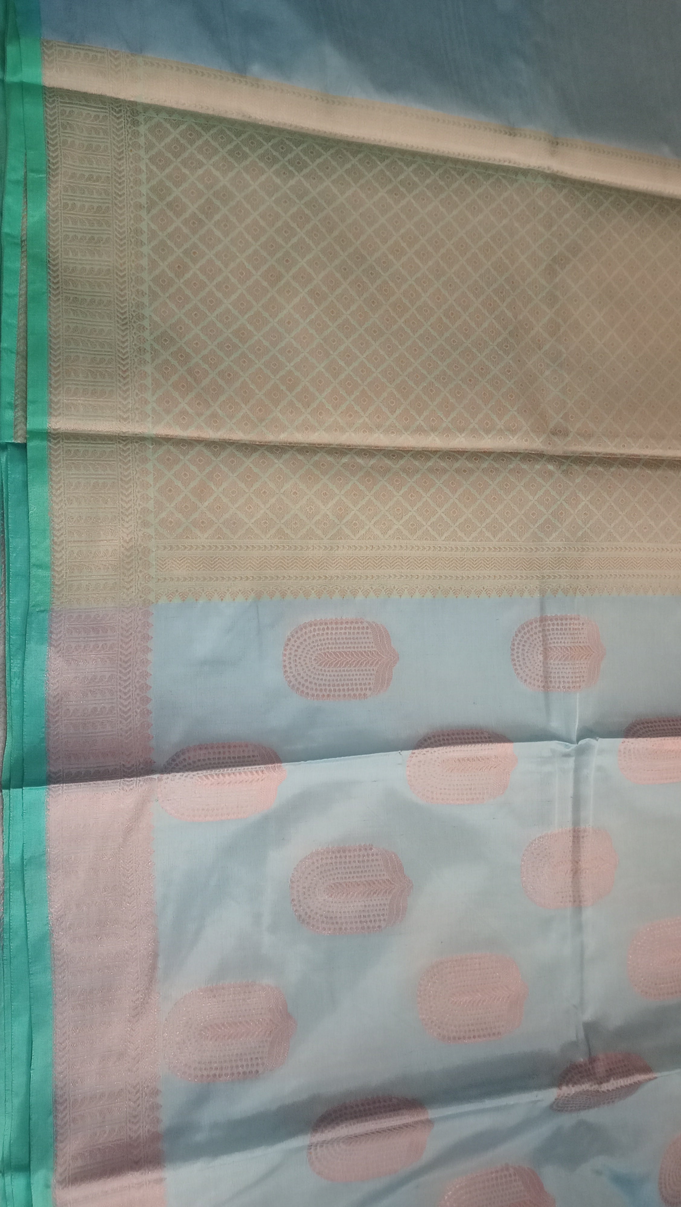 A close-up of a light blue and beige patterned saree, featuring pink oval designs and a green and silver border.